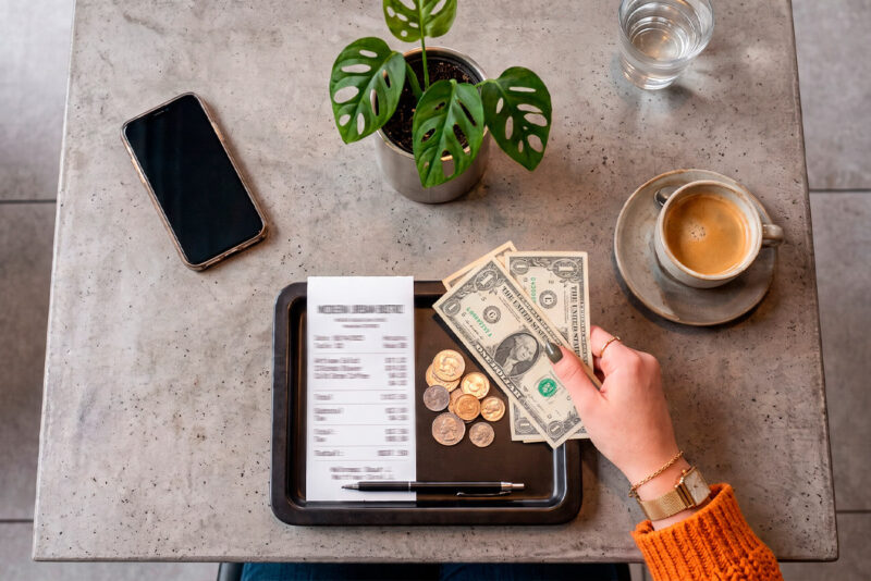 Mão deixando notas e moedas de gorjeta sobre a conta de um restaurante