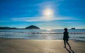 Mulher caminhando sozinha na praia ao nascer do sol — imagem inspiradora para post sobre frases de viagem para status e legendas.