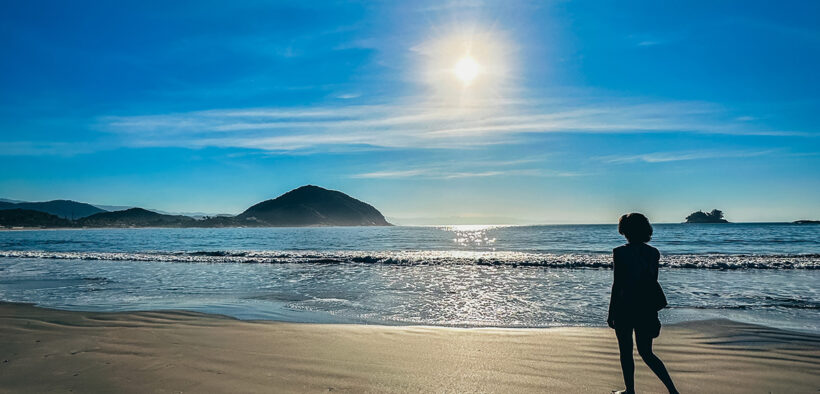 Mulher caminhando sozinha na praia ao nascer do sol — imagem inspiradora para post sobre frases de viagem para status e legendas.
